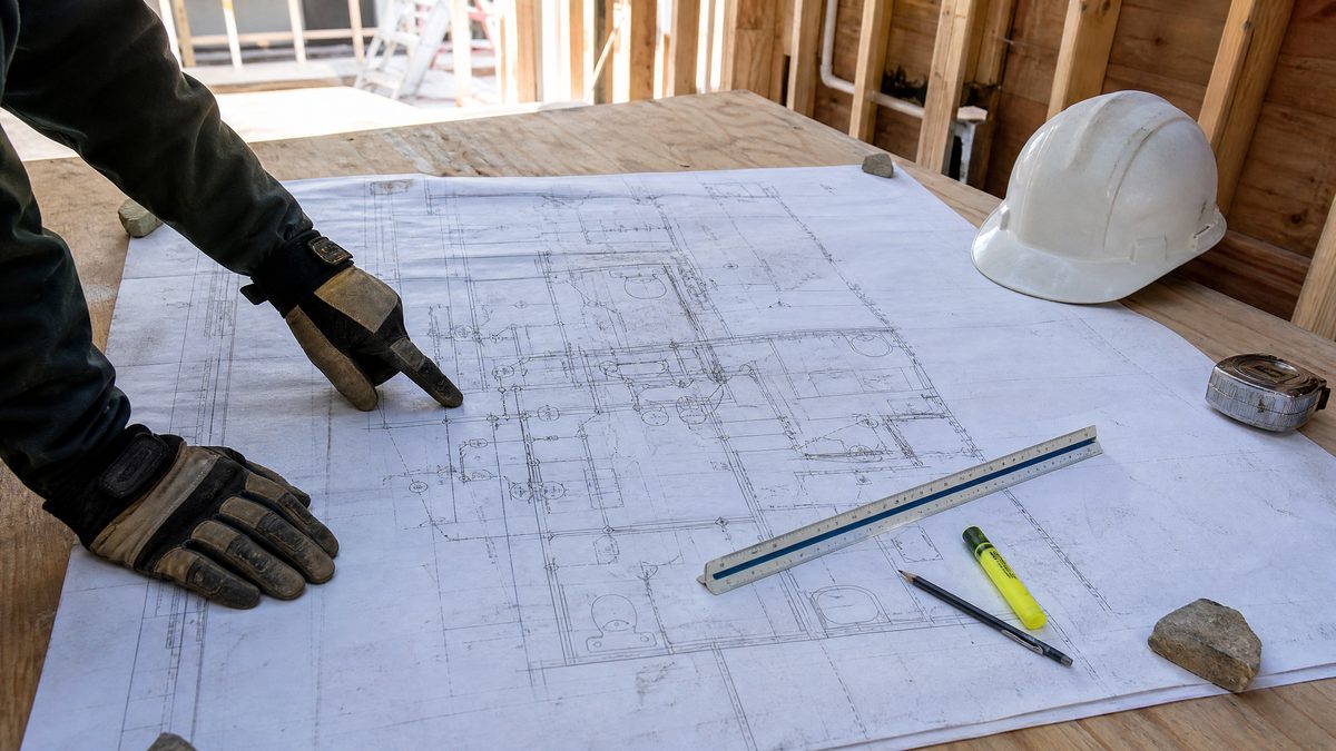 Plumbing contractor reviewing an architectural plan set on a job site table to price a new construction takeoff