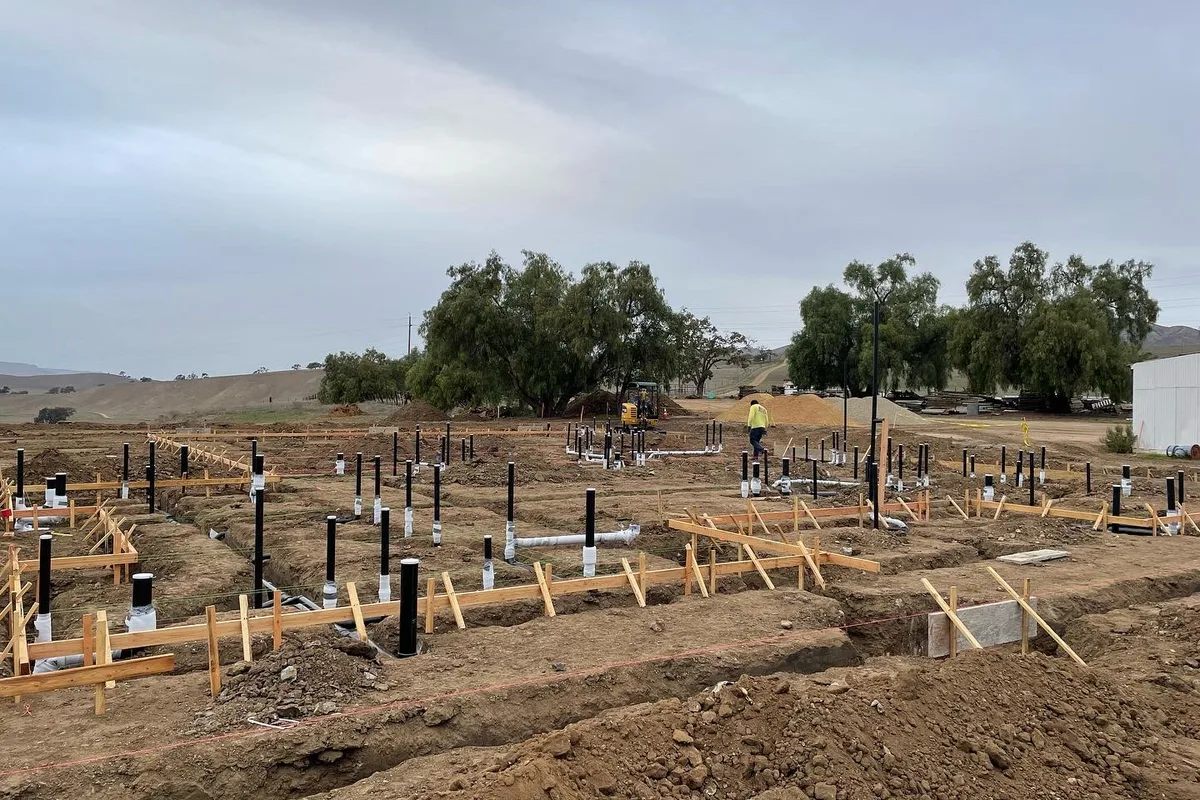 Ground-up commercial underground plumbing placed, risered, and staged for inspection before the pour.